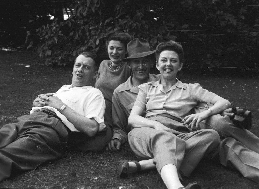 A black and white photo of four people laying on the grass
