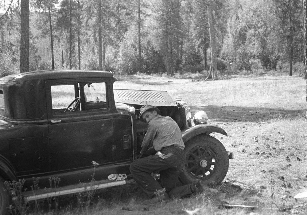 A black and white photo of a man working on an old car.