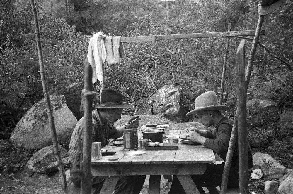 Two people are sitting at a picnic table in the woods.