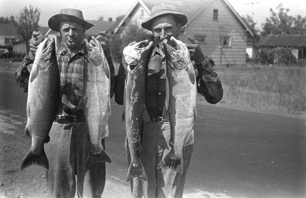 Two men are holding large fish in their hands in a black and white photo.