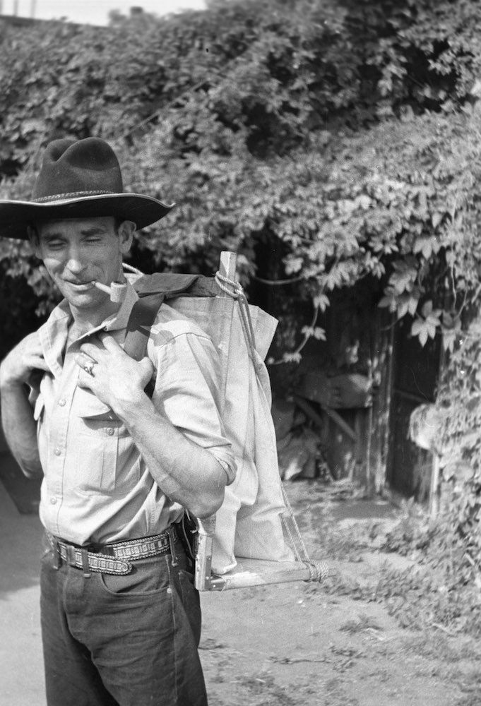 A man wearing a cowboy hat is carrying a bag on his back.