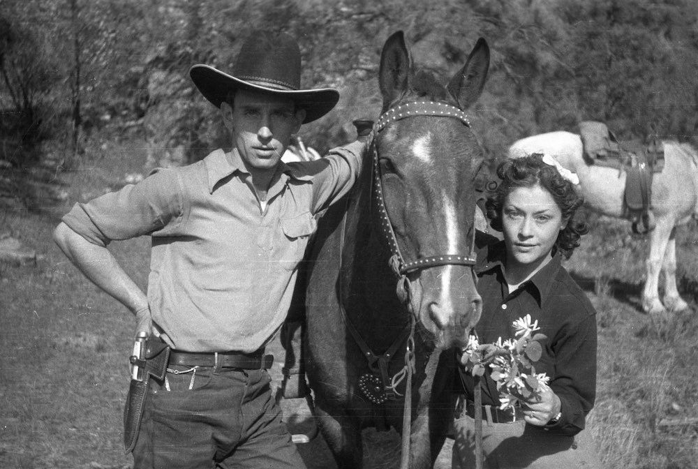 A black and white photo of a man and woman standing next to a horse.