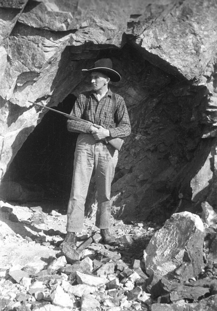 black and white photo of a man holding a rifle near a cave