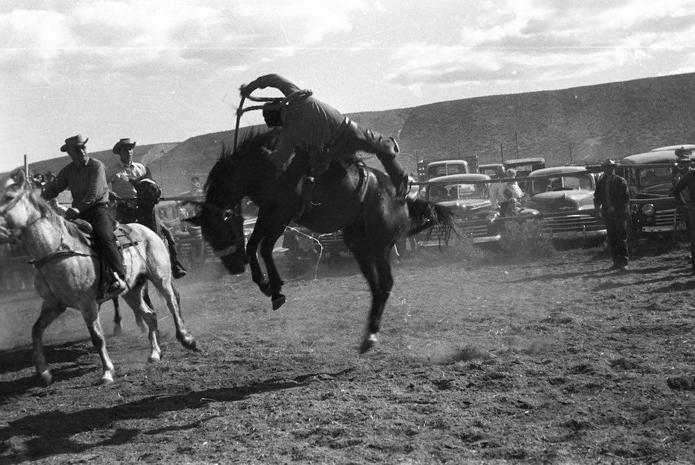 A black and white photo of a man riding a bucking horse