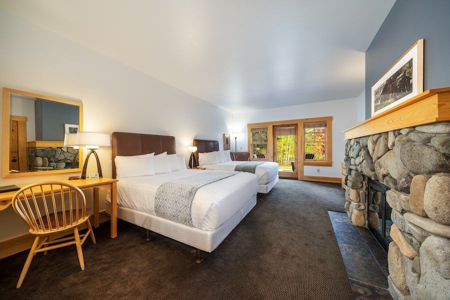 A hotel room with two beds , a desk and a fireplace.