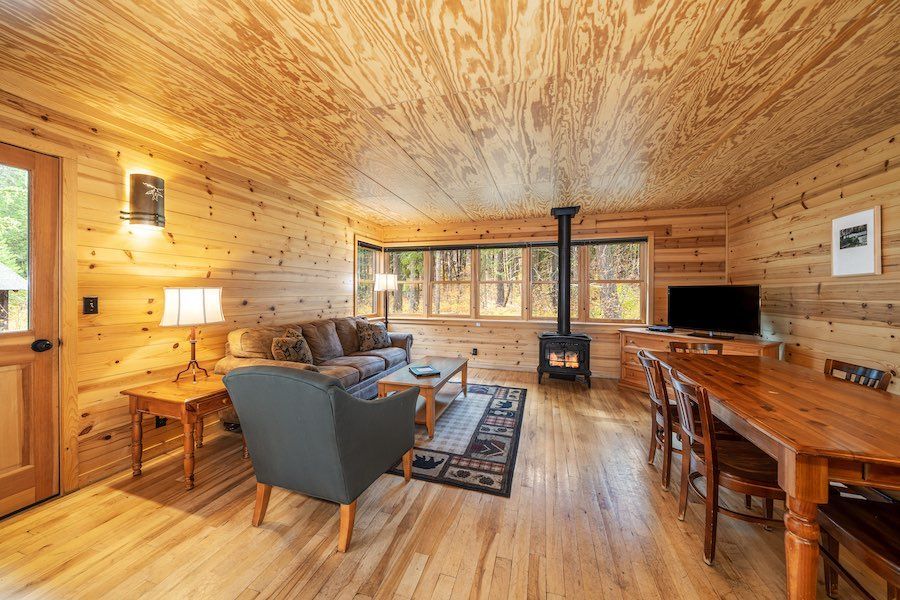 A living room in a log cabin with a couch , chairs , table and television.