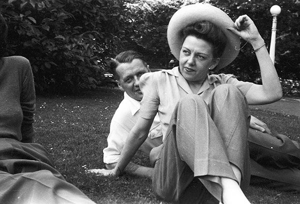 A woman wearing a hat is sitting on the grass with two other people