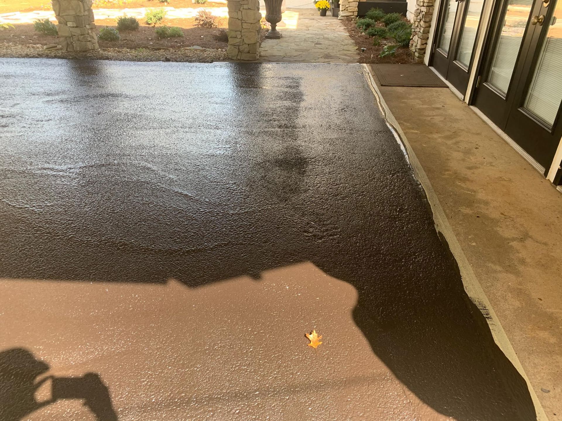 A wet, dark asphalt surface beside a building entrance with concrete steps and a glass door.