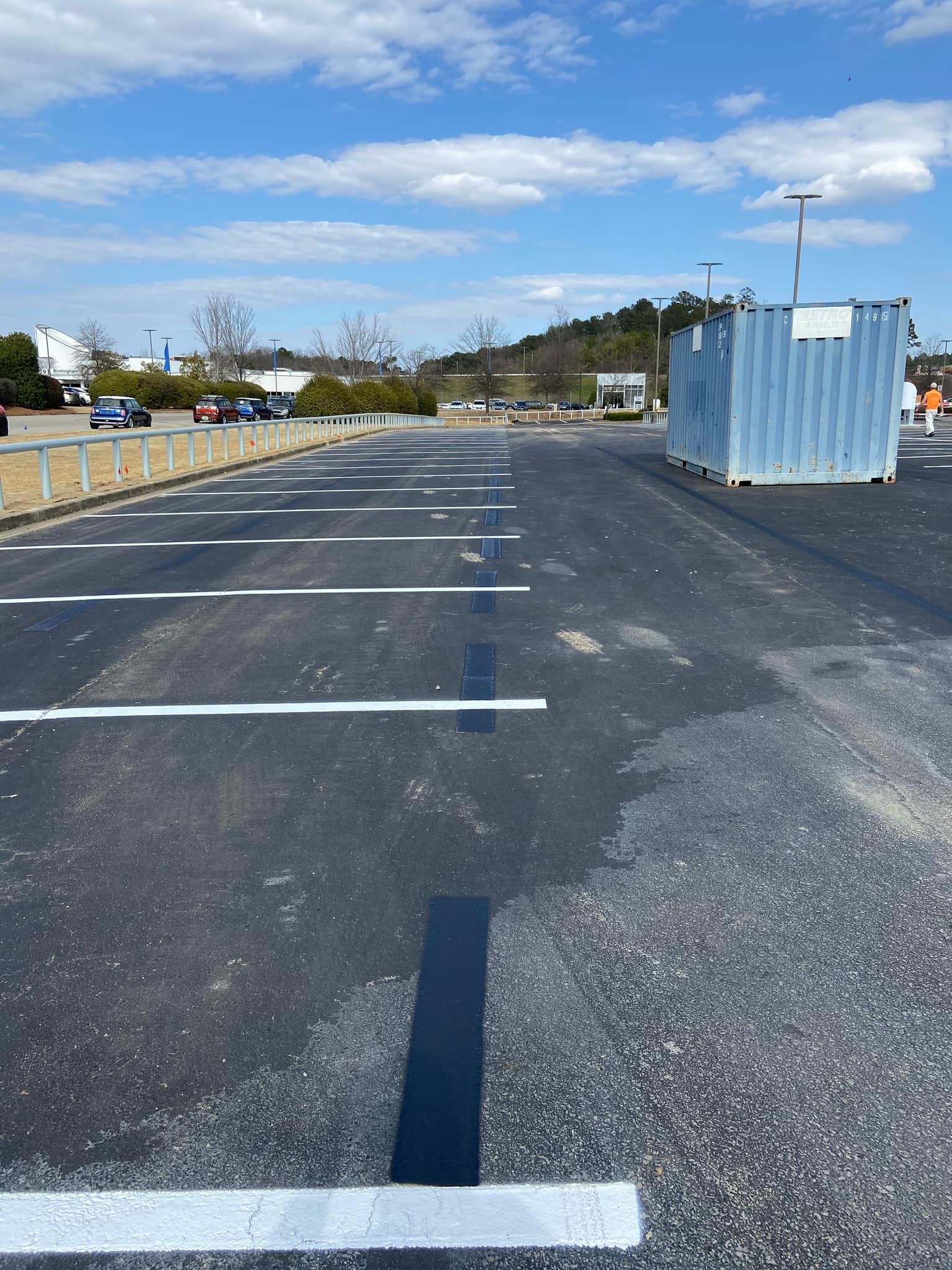 An empty asphalt parking lot with white painted lines and a large, light blue shipping container on the right.