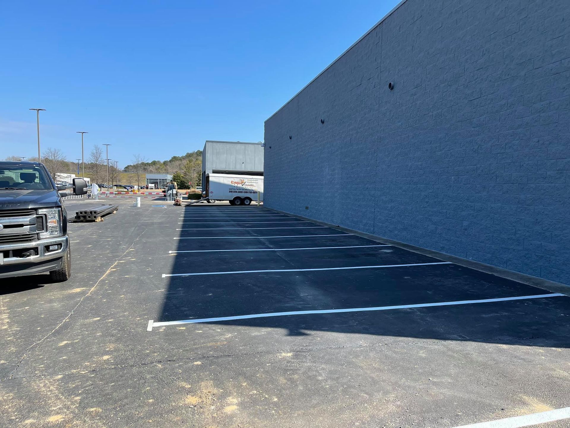 A parking area with newly painted white stripes along a long, blue exterior wall under a clear blue sky.