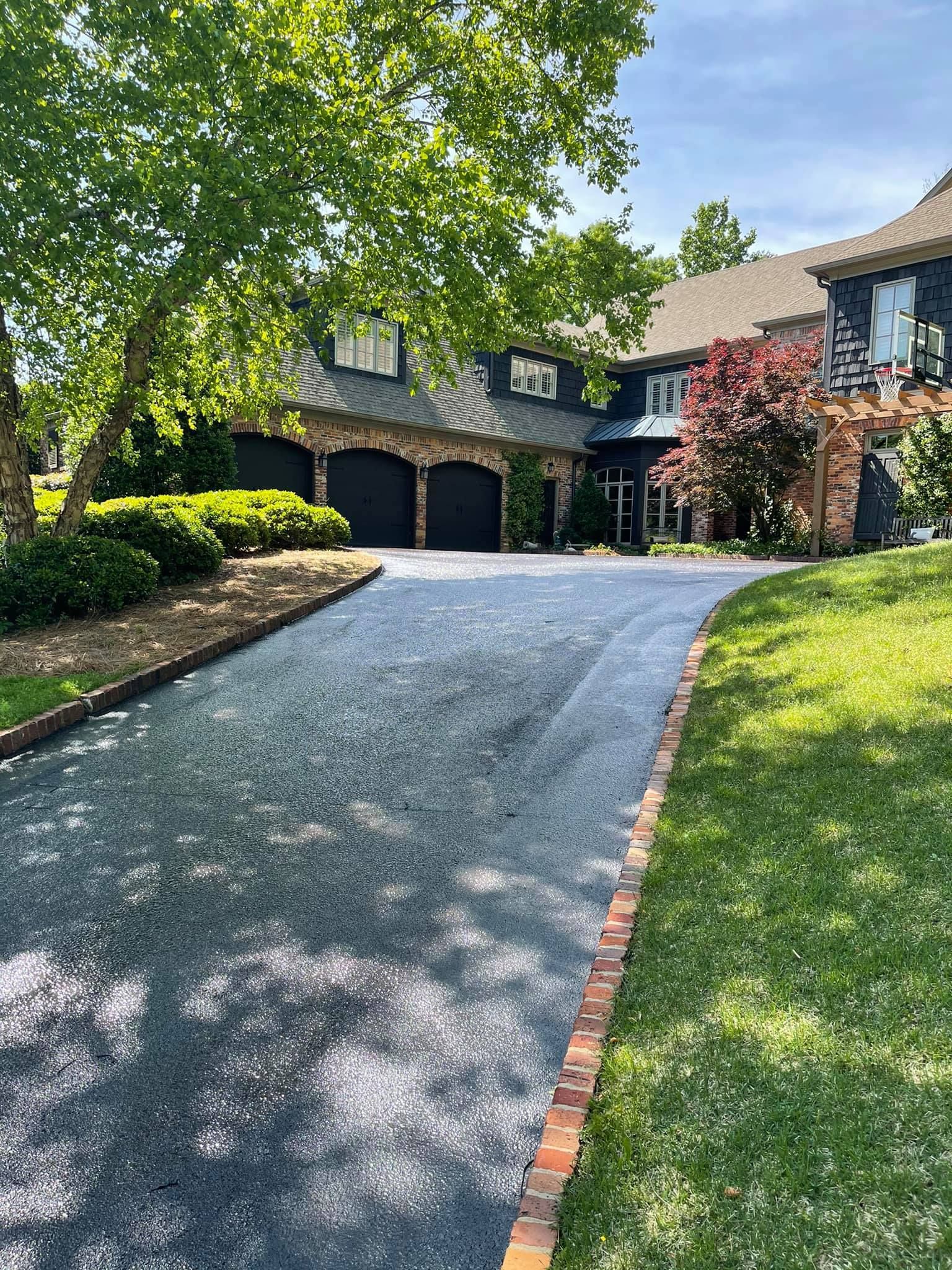 A long gravel driveway leads to a large, multi-story home with a three-car garage, brick accents, and a lush front lawn.
