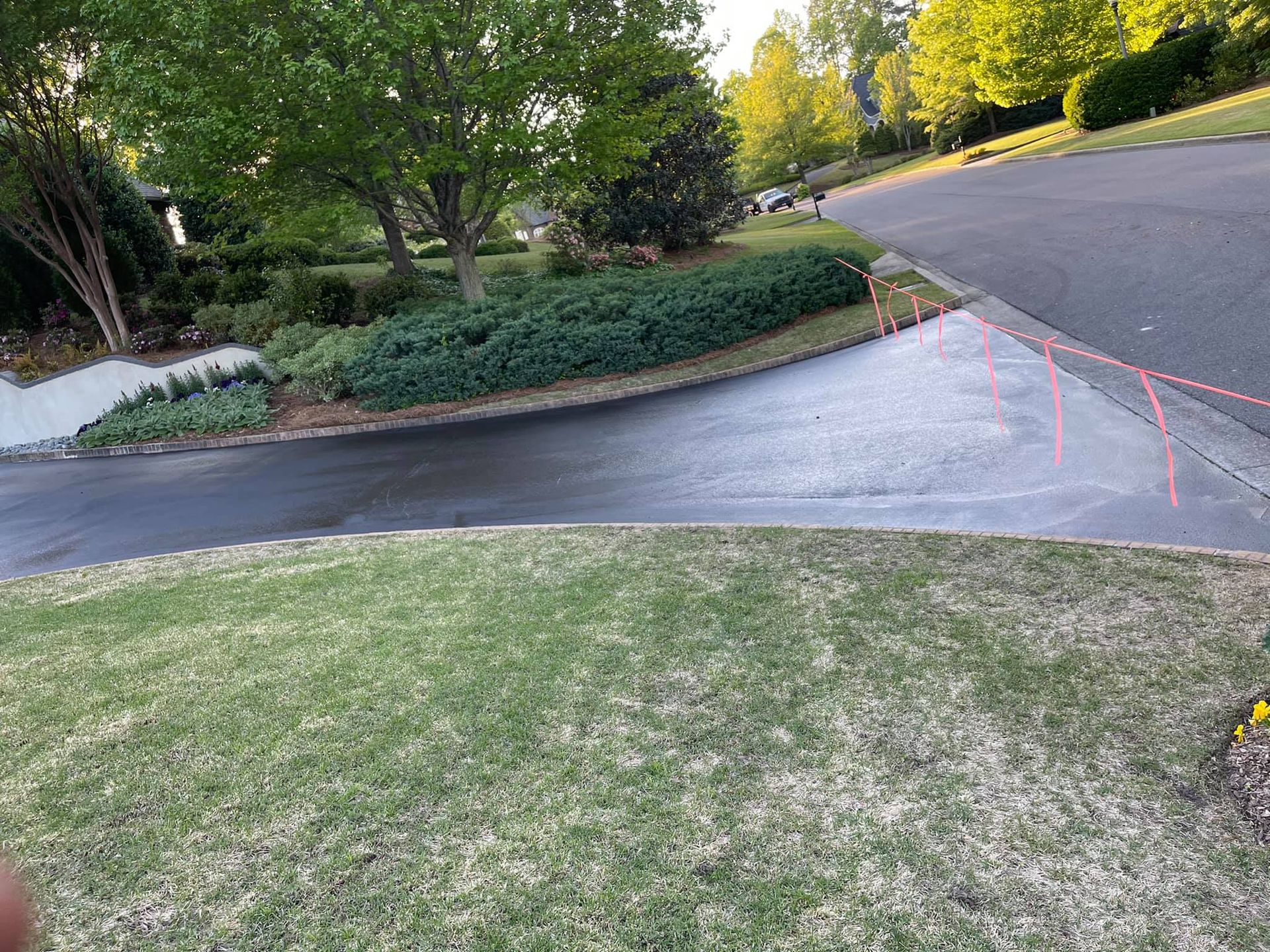 A paved driveway entrance meeting a road with orange survey flags placed along the curb line in a residential yard.