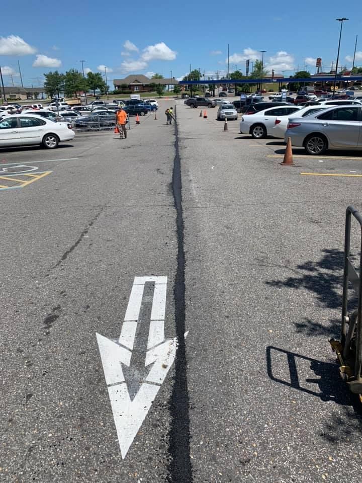 A parking lot with a painted white arrow pointing toward a lane marked by orange safety cones and a long crack.