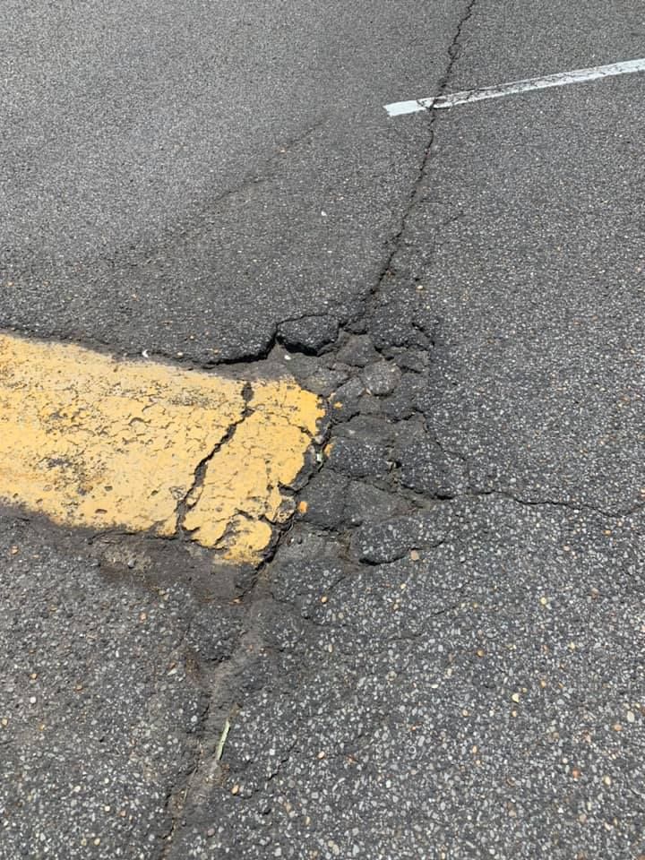A pothole in asphalt near yellow and white painted parking lines.