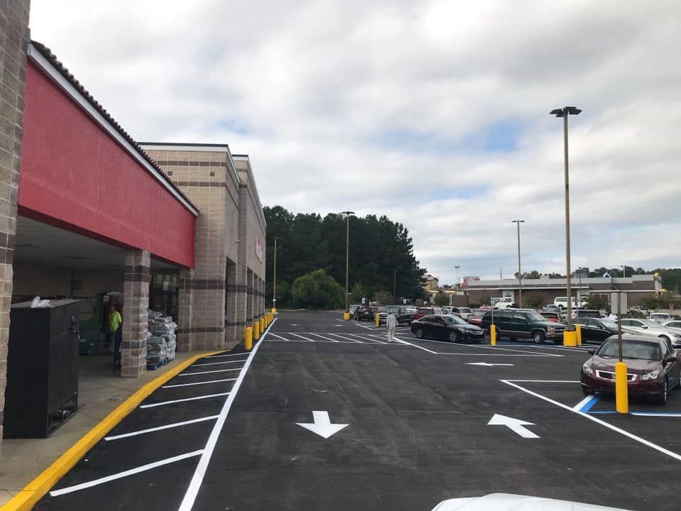 A red-facaded retail building alongside a newly paved parking lot with white directional arrows and marked spaces.