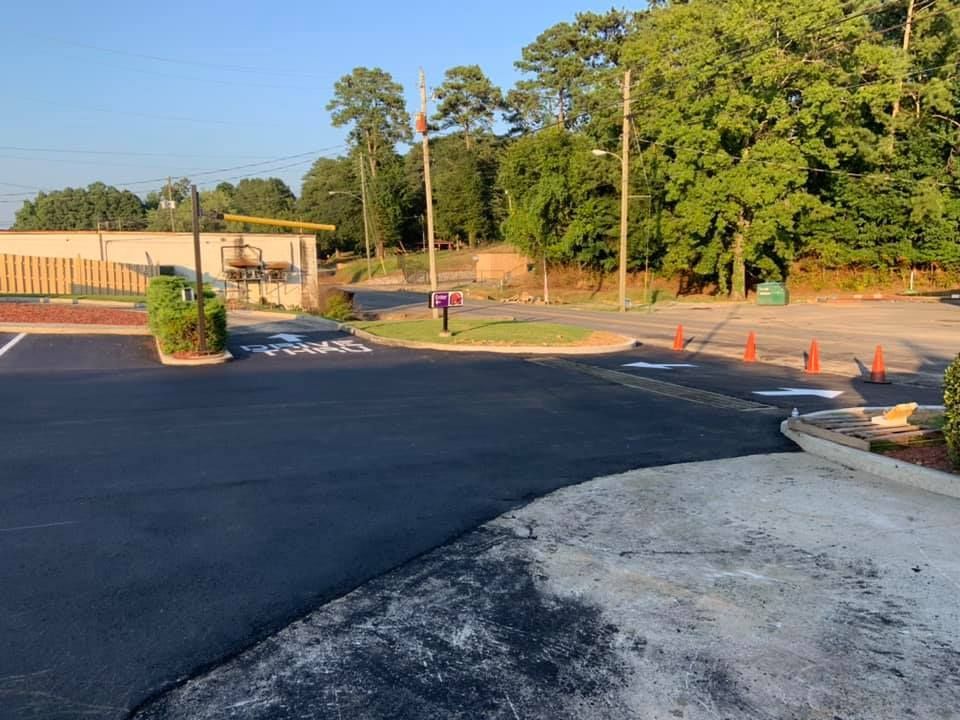 Freshly paved asphalt driveway leading to a commercial building, marked with white arrows and orange traffic cones.