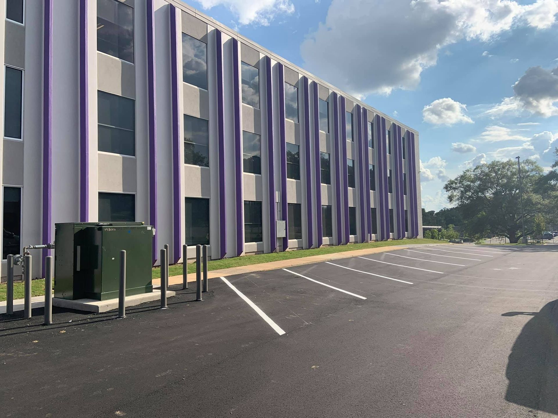A modern office building with white exterior walls and vertical purple architectural accents beside a paved parking lot.