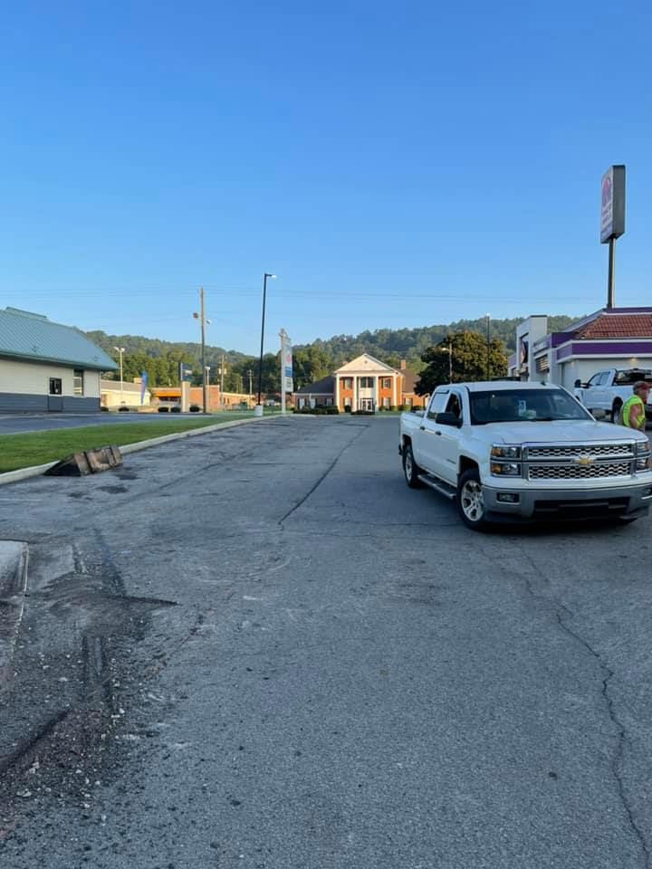 A white pickup truck parked in an asphalt lot with a building and hills in the background under a clear blue sky.