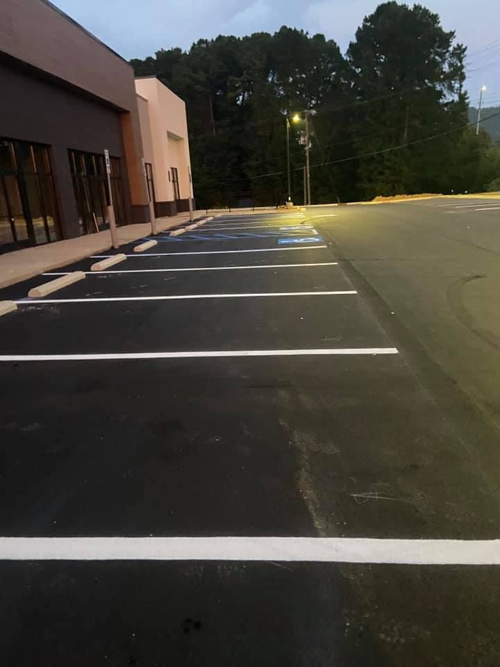 Freshly paved parking lot with white painted lines and directional arrows, located in front of a modern warehouse building.