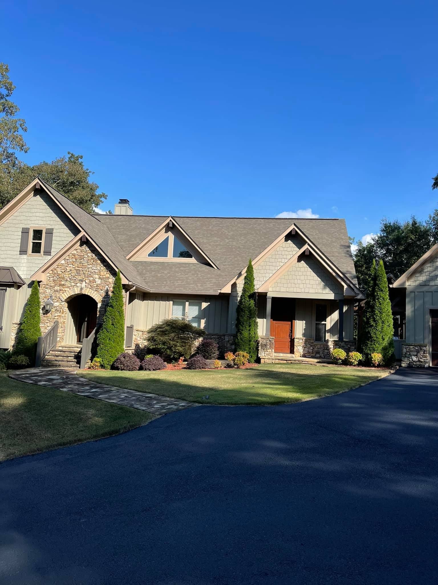 A single-story home with a stone-accented front, a grey shingled roof, a front porch, and surrounding landscaping.