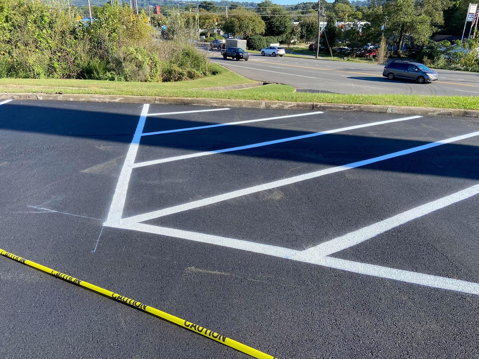 Newly painted white chevron pavement markings in a parking lot, with a yellow caution tape line across the foreground.
