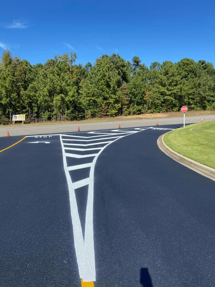 Freshly paved road with white lane markings, including a chevron-patterned painted island, leading to a stop sign.