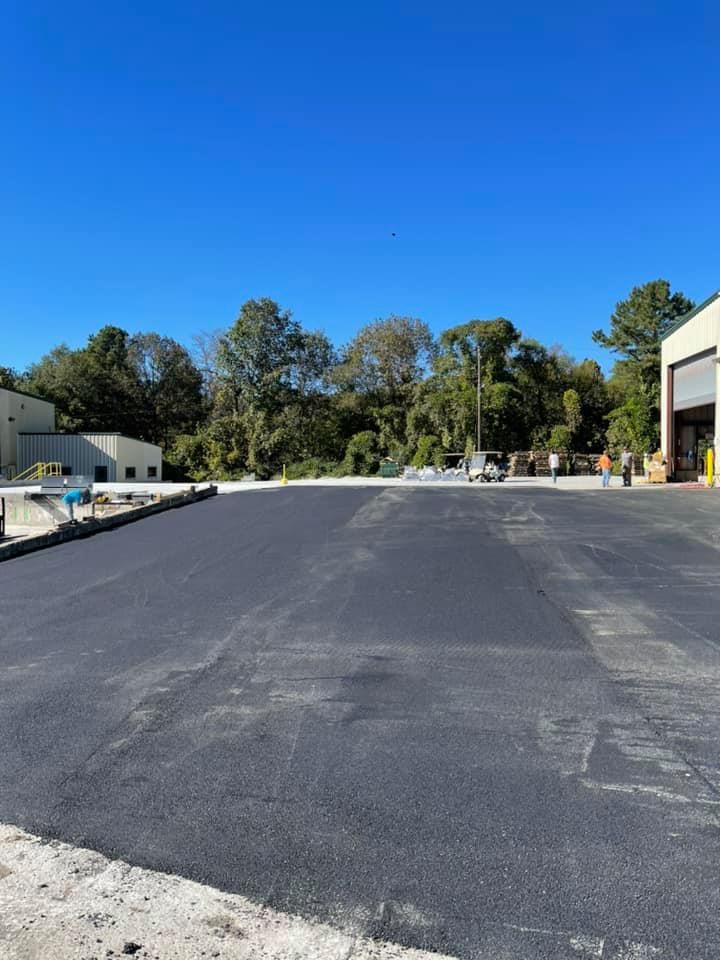 Newly paved dark asphalt lot with light-colored building edges under a clear blue sky.