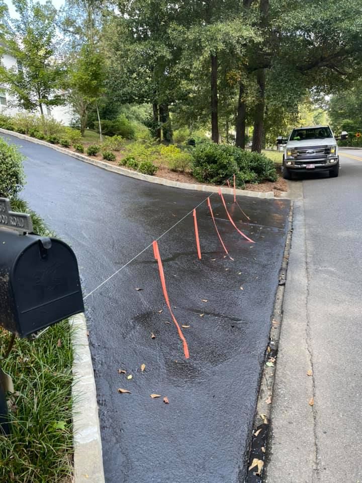 A newly paved driveway with a line of bright orange surveyor flags, a mailbox, and a white pickup truck in the background.