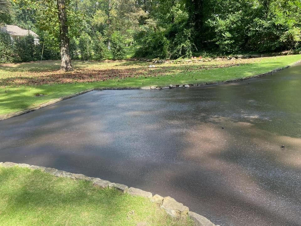 A paved driveway bordered by stone edging, leading toward a grassy yard with trees in the background.