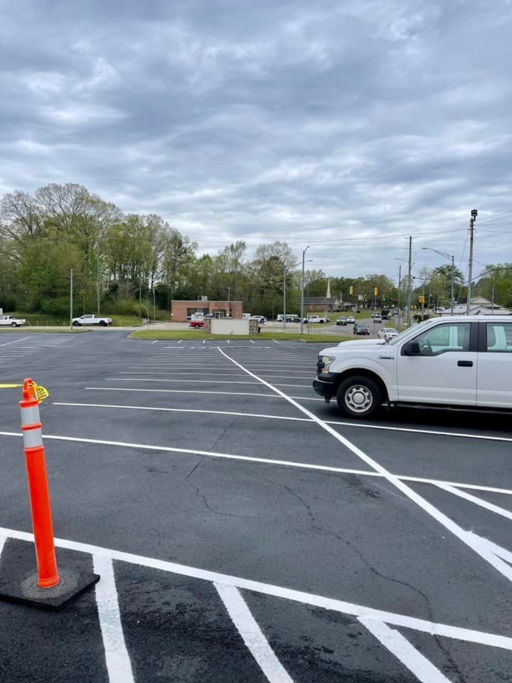 A white truck parked in an empty parking lot with striped painted lanes and an orange traffic cone in the foreground.