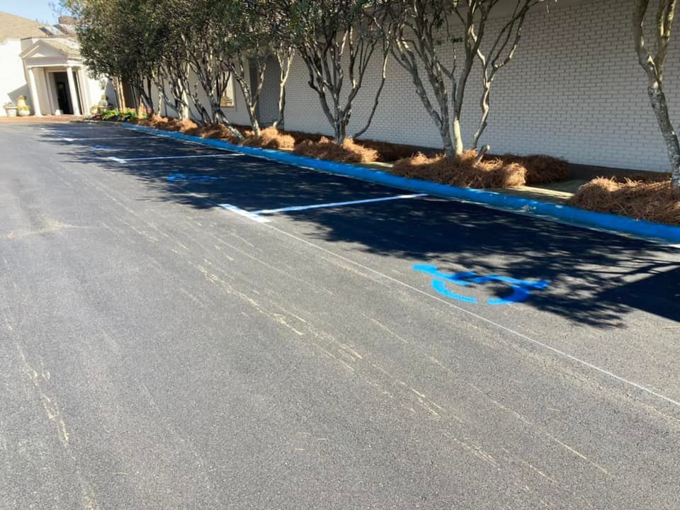 Empty parking spaces with blue painted handicap symbols and curbs in front of a white building with trees.