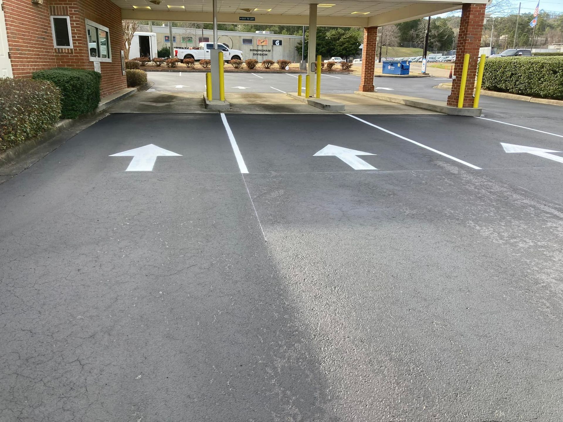 A drive-thru lane with three lanes marked by white directional arrows leading toward a brick building canopy.