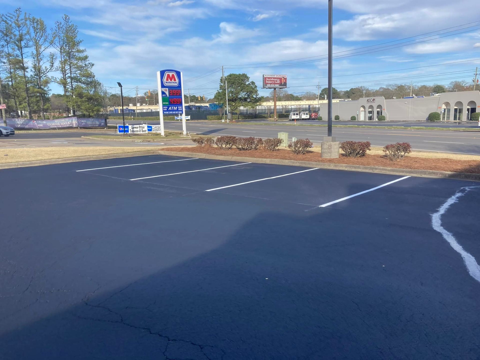 An empty parking lot with freshly painted white lines on asphalt, featuring a gas station sign in the background.