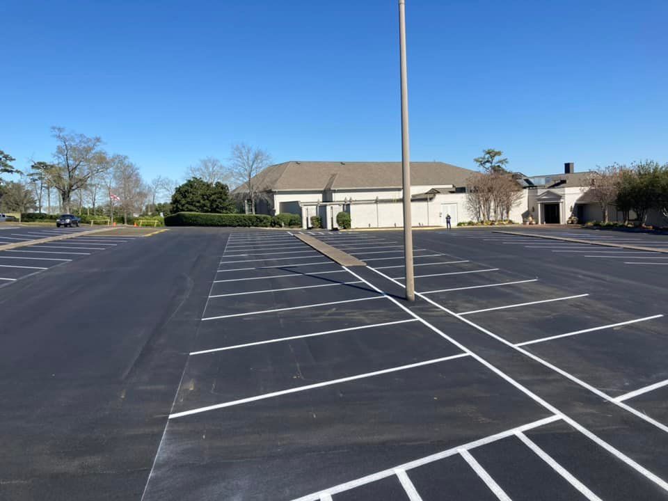 Empty parking lot with freshly painted white lines and a tall light pole in the center on a clear, sunny day.