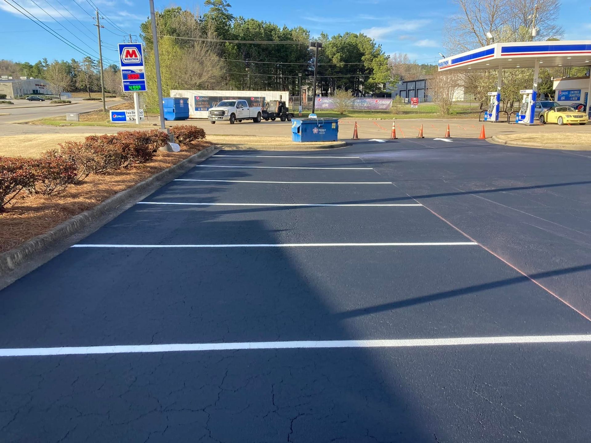 Freshly paved parking lot with white-painted lines and a gas station in the background.