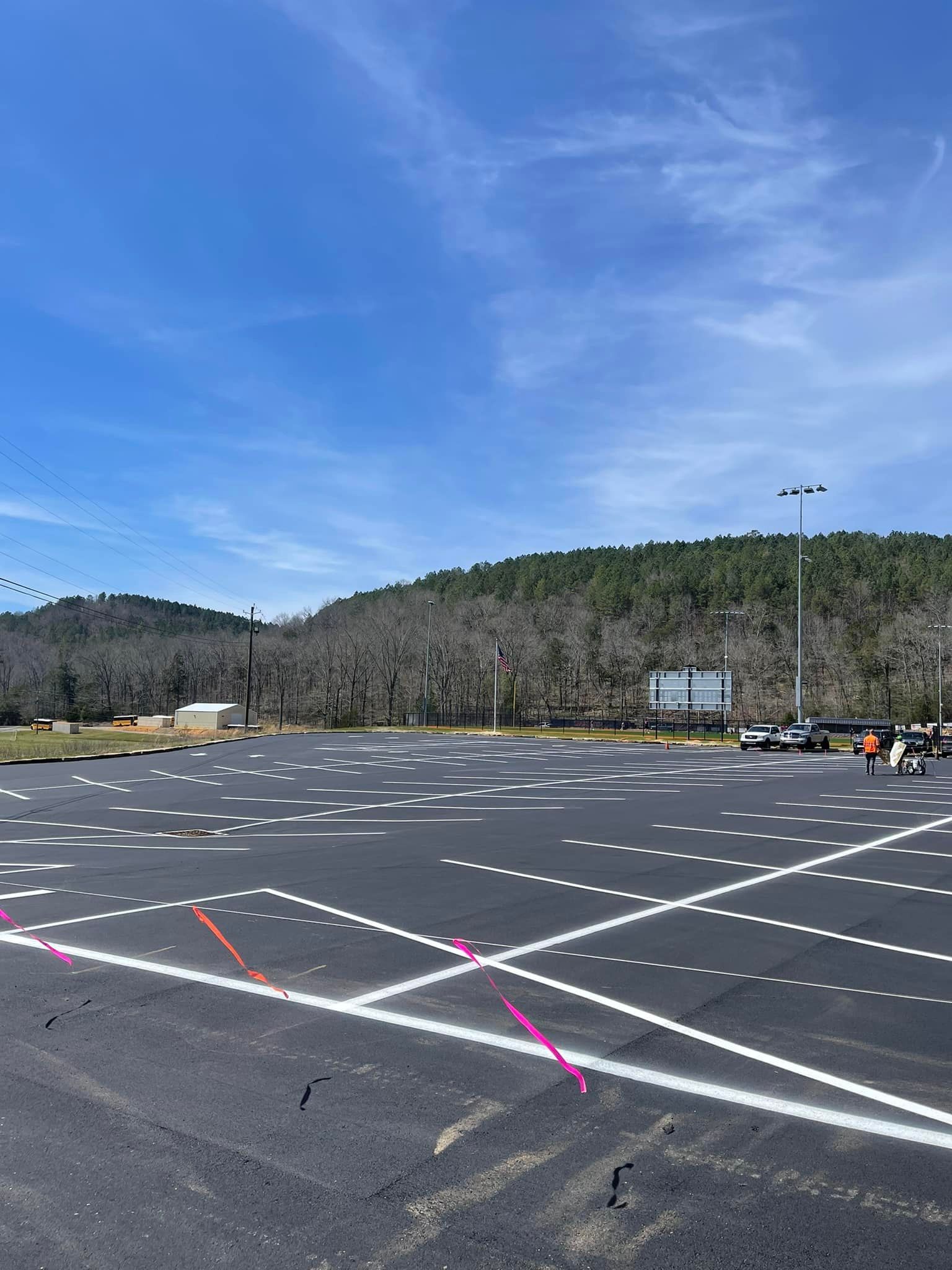 Newly paved parking lot under a bright blue sky, featuring fresh white parking space lines marked with pink survey tape.