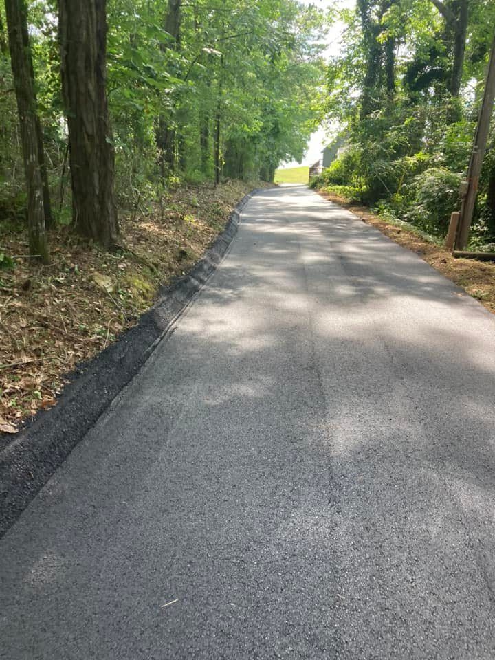 A newly paved asphalt road flanked by trees and woods, leading into the distance.