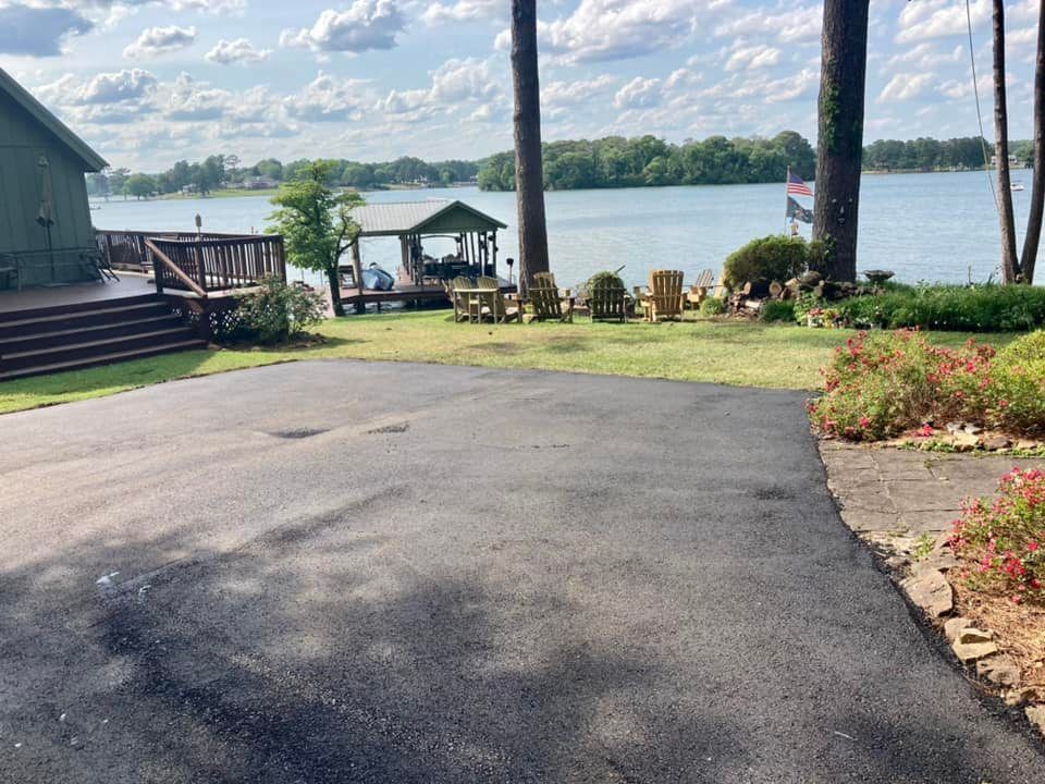 A paved driveway leads to a wooden deck, lawn, and boat dock overlooking a lake under a cloudy sky.