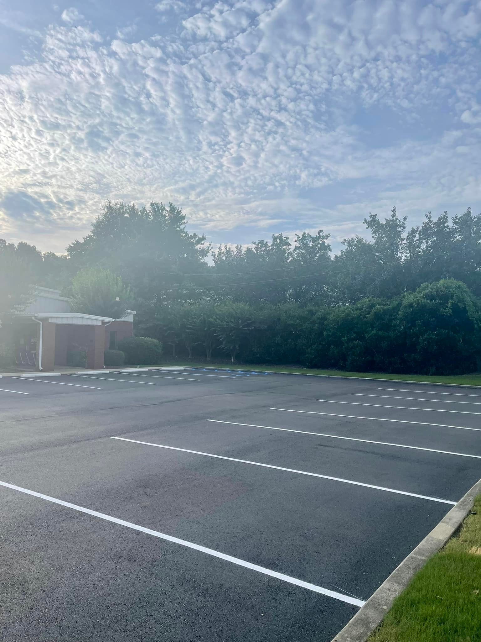 A paved parking lot with white dotted parking space lines under a bright, partly cloudy sky.