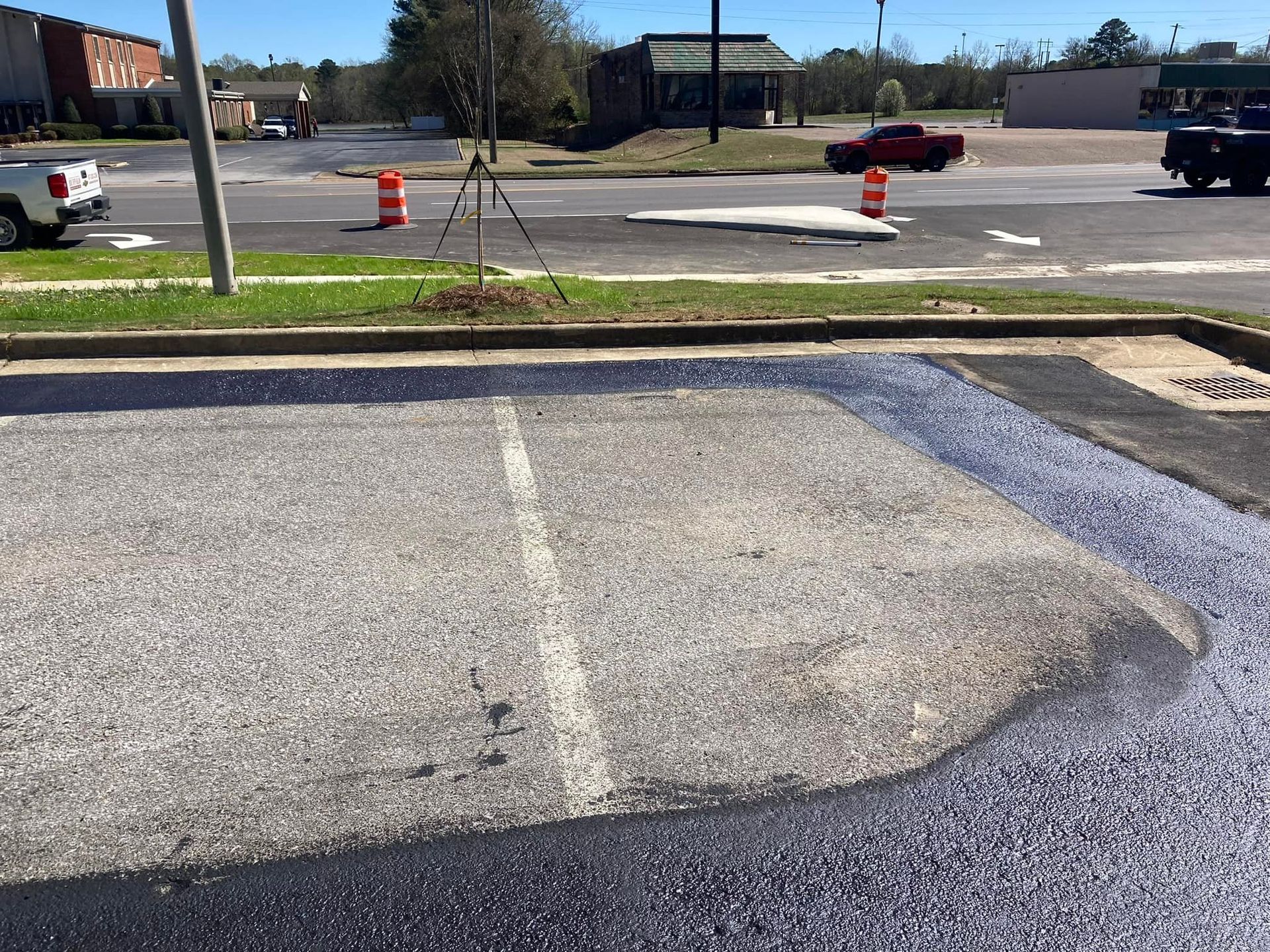 A partially repaved asphalt parking lot with fresh black sealant next to an older section, viewed near a street intersection.