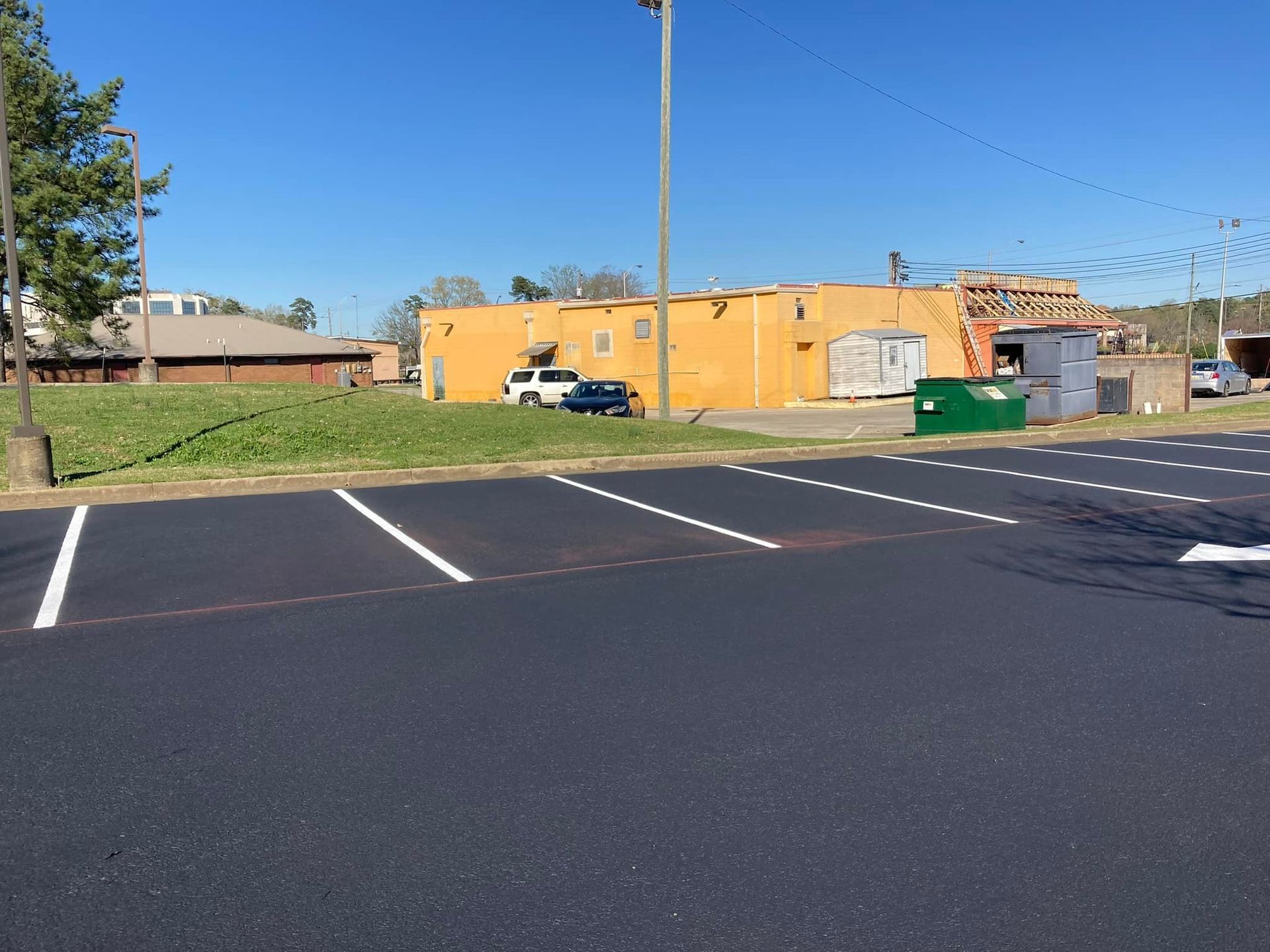 A newly paved parking lot with white painted lines in front of a yellow commercial building and grassy area.
