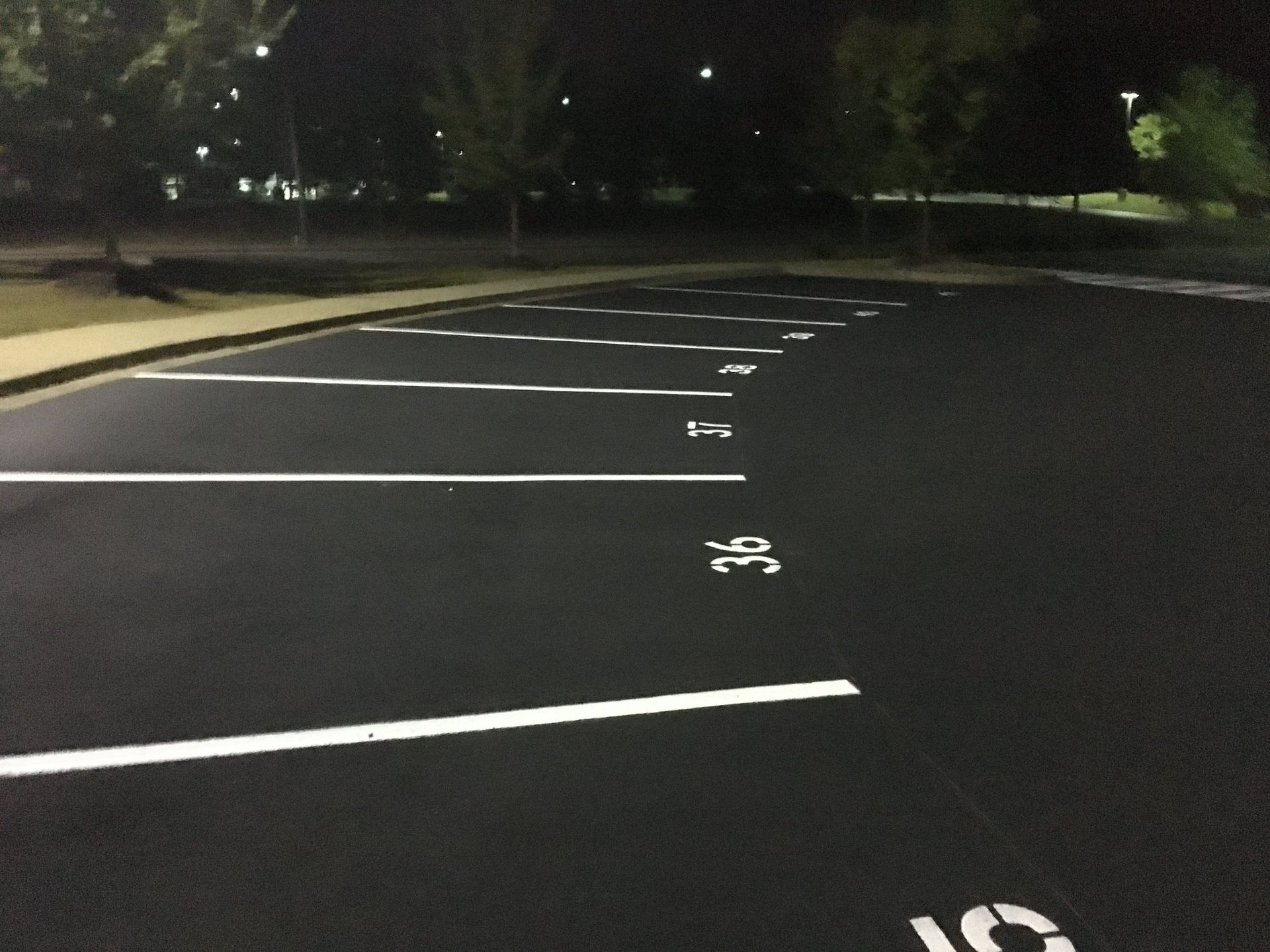 An empty parking lot at night with white-painted lines and numbered spaces under overhead lighting.