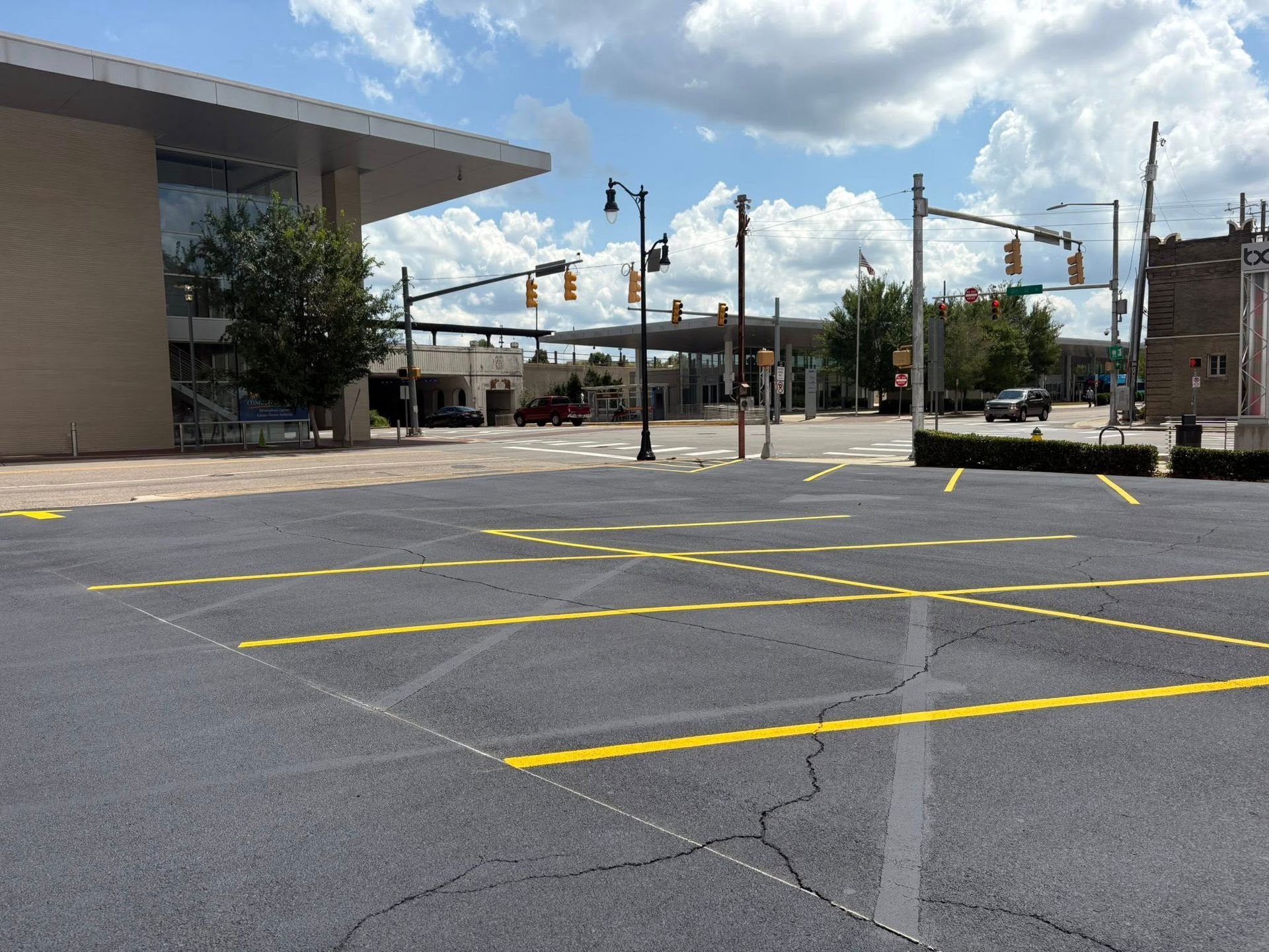 An empty parking lot with yellow-painted lines in front of a modern building and an intersection with traffic lights.