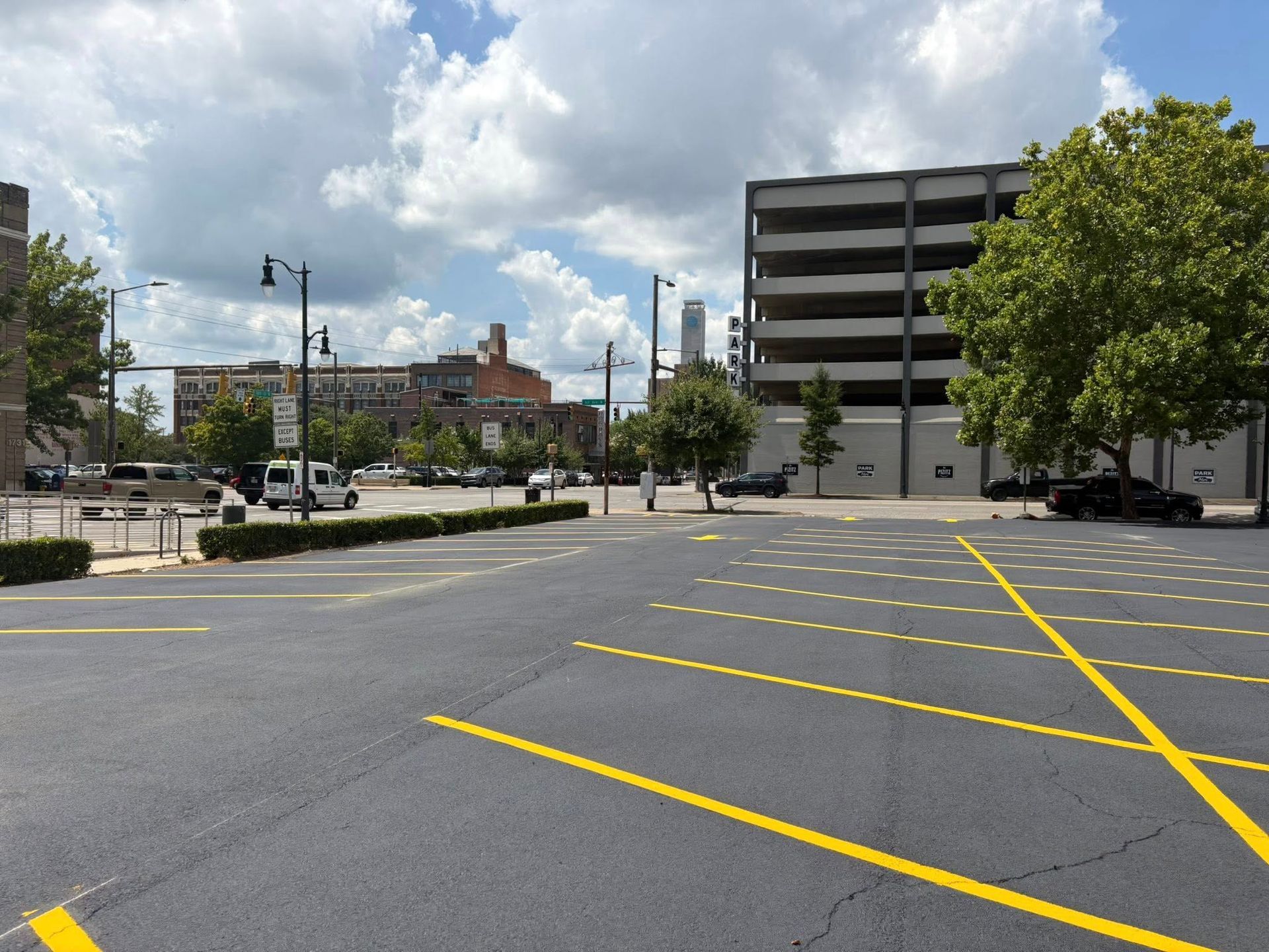 A freshly paved parking lot with white painted lines and a grass verge under a clear blue sky.