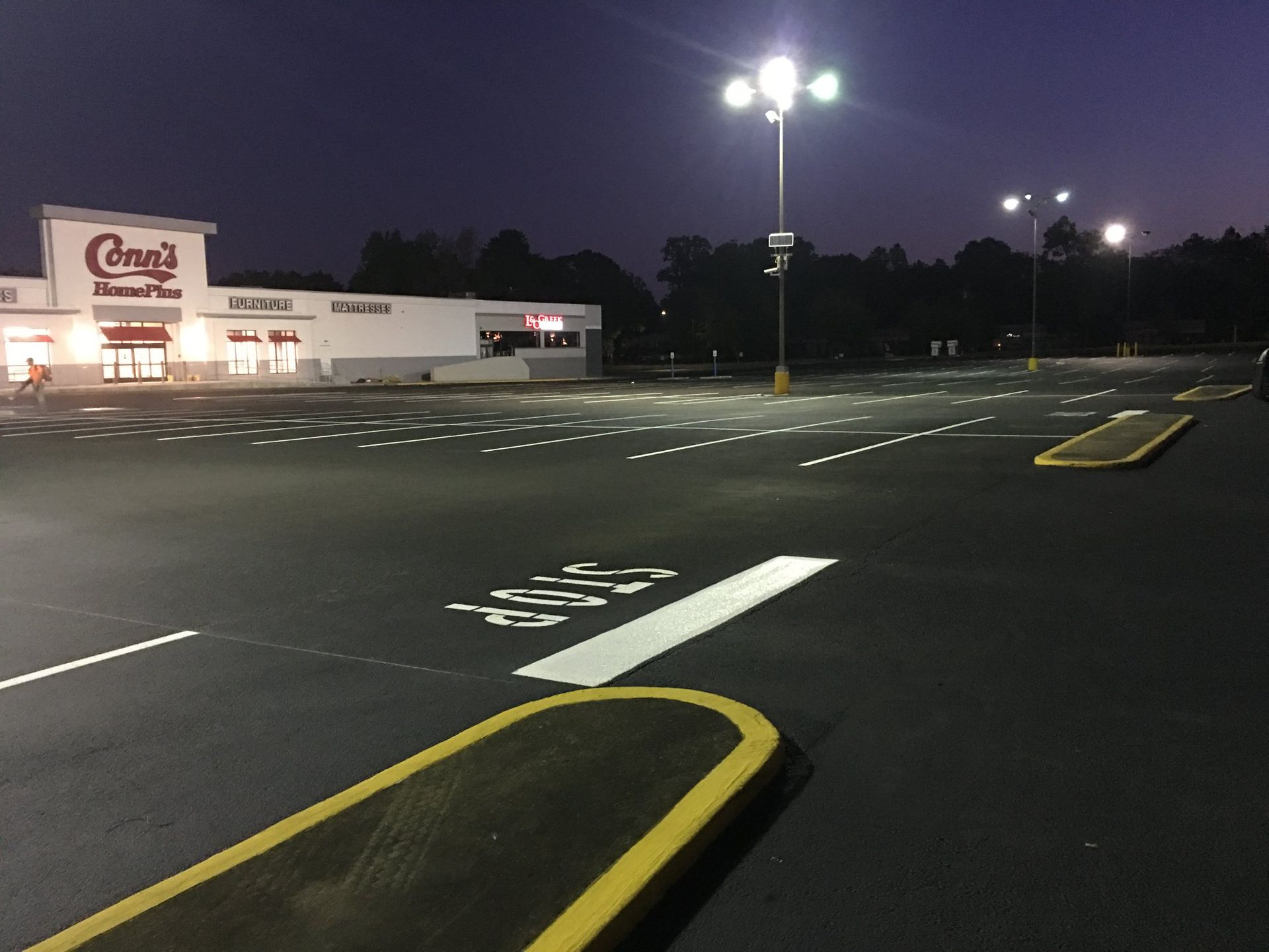 An empty parking lot with white painted stall lines and a yellow-striped pedestrian crossing on dark gray asphalt.