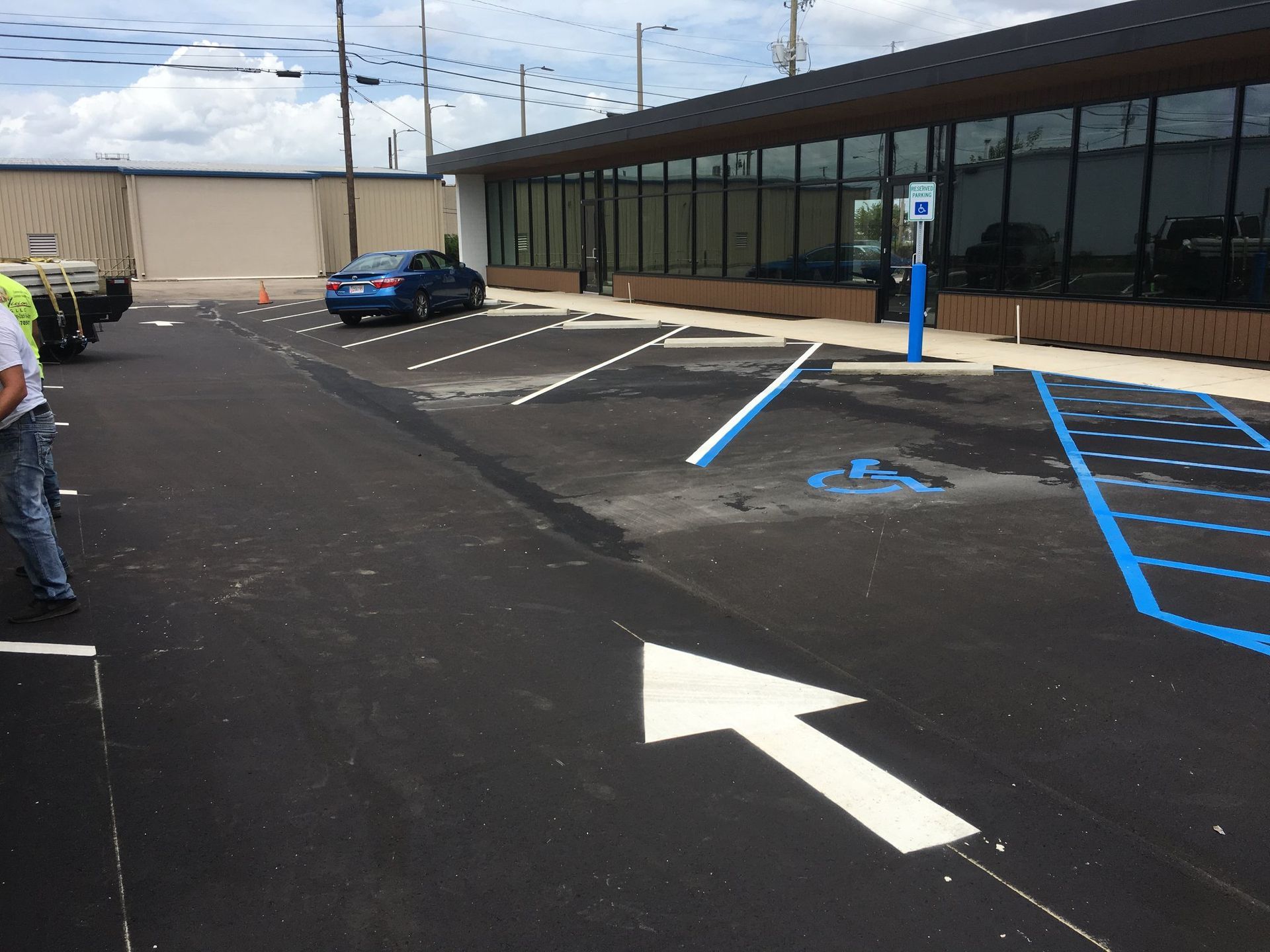 A freshly paved parking lot featuring a blue-marked handicap accessible space, a directional arrow, and a modern building.