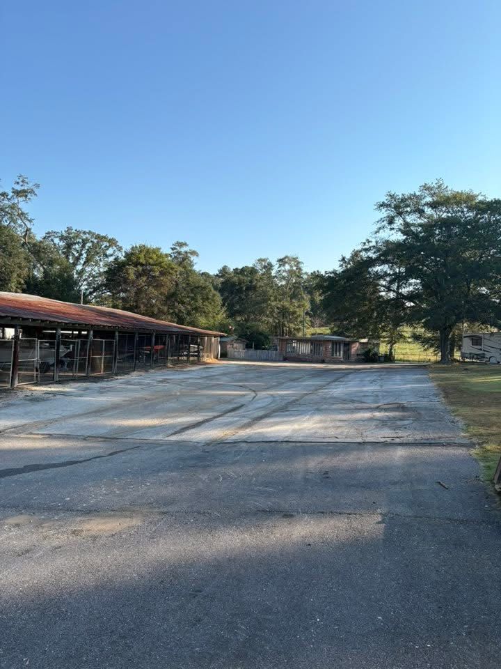 An empty, cracked asphalt lot in front of a long, open-sided wooden structure with a metal roof under a clear blue sky.