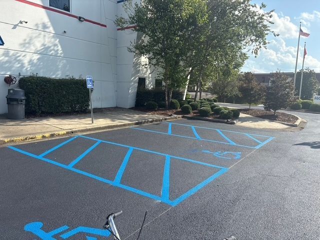 A designated blue and white accessible parking space and loading zone in a paved lot next to a white building.