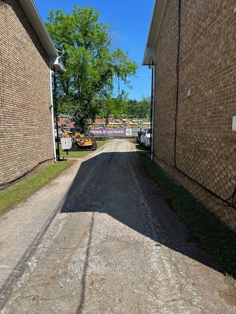 A paved driveway runs between two brick buildings toward a tree and a banner that reads 