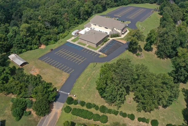 Aerial view of a commercial building surrounded by parking lots and dense forest with a gated entrance road.